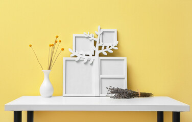 Family tree with photo frames and flowers on table near yellow wall