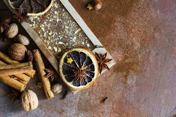 Christmas chocolate with orange peel and spices. Composition with cinnamon sticks; anise , nutmeg, cloves, hazelnut and dried orange slices on dark background. Copy space for your text. 