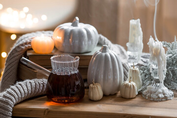 Still-life. Pumpkins, old books, hot tea, a blanket and burning pumpkin-shaped candles on a wooden table in a cozy living room. Home autumn concept.