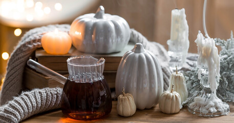 Still-life. Pumpkins, old books, hot tea, a blanket and burning pumpkin-shaped candles on a wooden table in a cozy living room. Home autumn concept.