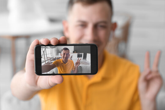 Young man showing victory gesture while taking selfie at home, closeup