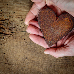 Zwei Hände halten ein Herz aus rostigem Stahlblech vor rustikalem Eichenholzbrett.