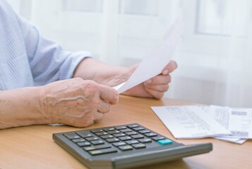 
Close-up of an elderly man's hands holding a bill for gas, water and counting on a calculator. Rising prices for energy resources. Selective focus on the hand.