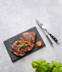 BBQ grilled beef steak with pepper,  rosemary and basil on black slate on light  background.