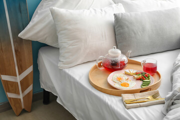 Wooden tray with tasty breakfast and hot tea on bed