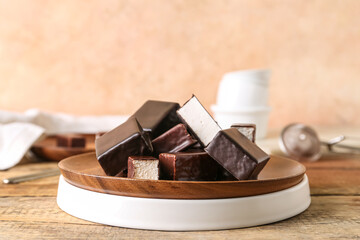 Plate with tasty bird's milk candies on wooden table