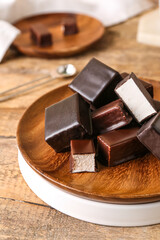 Plate with tasty bird's milk candies on wooden table, closeup