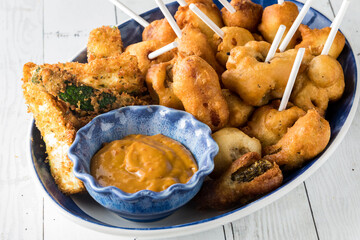 A close up of a platter of deep fried appetizers served with hot mustard.