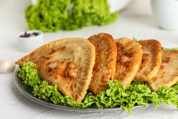 Plate with tasty chebureks and lettuce on light background, closeup