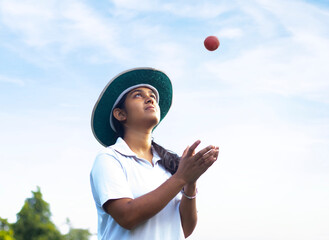 Girl wearing cricket uniform catching the ball on the field