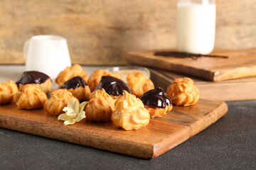 Wooden board with delicious eclairs on table