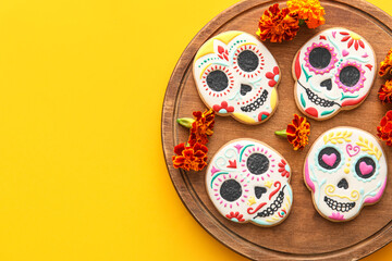 Fototapeta na wymiar Board with skull shaped cookies and flowers on yellow background. El Dia de Muertos