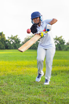 Female cricket player wearing protective gear and hitting the ball with a bat on the field