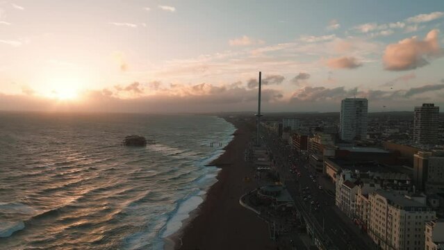 Magical sunset 4k aerial video of British Airways i360 viewing tower pod with tourists in Brighton, UK with sea and Brighton Palace Pier in the background.