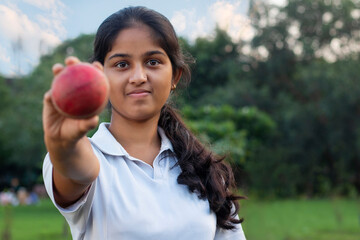 Girl wearing cricket uniform showing ball on the field - obrazy, fototapety, plakaty