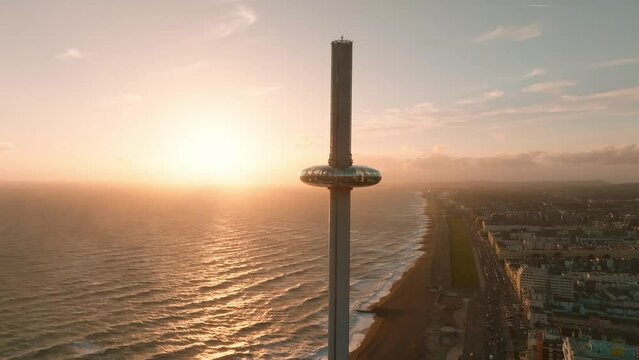Magical sunset 4k aerial video of British Airways i360 viewing tower pod with tourists in Brighton, UK with sea and Brighton Palace Pier in the background.