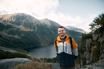 Happy tourist on the top of the mountain against beautiful lake and forests on the hills. Concept of easy hike during the weekend. Hiker smiles and looks at the camera.