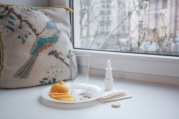 Seasonal cold: an empty glass cup, sliced lemon, instant pills and nasal spray with paper napkins...