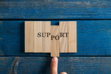 Male finger assembling a Support sign spelled on wooden pegs
