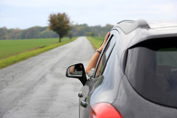Dłoń kobiety, ręka wysunięta przez okno samochodu osobowego, suwa, na drodze przez pola.