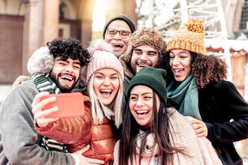 Multicultural happy friends having fun taking group selfie portrait on city street in a winter day - Multiracial young people celebrating laughing together outdoors - Happy lifestyle concept.