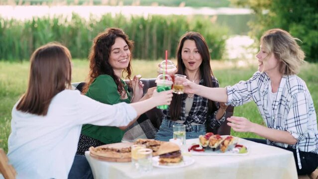 Girlfriends are having fun. Four young cheerful women eat and drink drinks in nature. The female tells her friends a funny story.