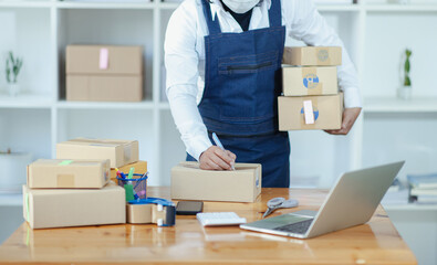 A young man running a small SME business uses a smartphone. laptop and calculator
To check the SME packaging box, the concept of the e-commerce team. sell products online