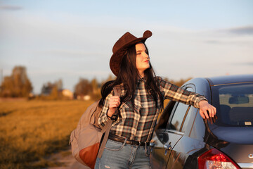 A young girl is traveling around the city hitchhiking. A beautiful young girl went on vacation. A female student in a cowboy hat on the road in autumn.
