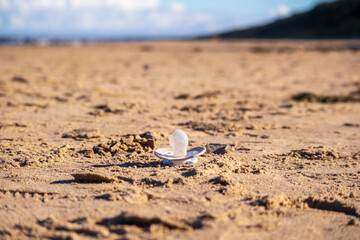 A white binky laying in the sand with blue sky next to the sea