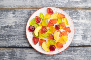 Various fruit candies on plate on gray wooden background. close up, top view.