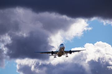 A big white airplane flying in the blue sky with many white and dark blue clouds