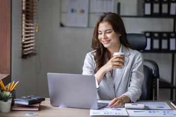 Beautiful young smiling asian multiethnic woman working on laptop and drinking coffee in at workplace, Asia woman working document finance and calculator in her home office. Enjoying time at home.