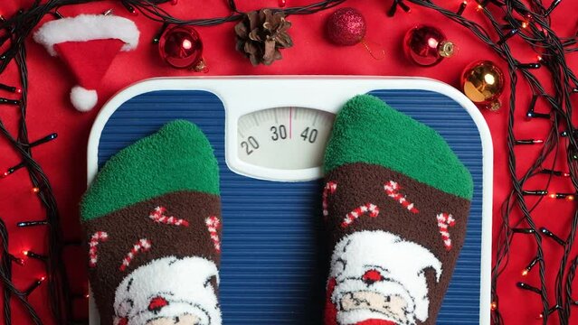 A woman in Christmas socks stands on the scales, weighs herself after gluttony during the holidays