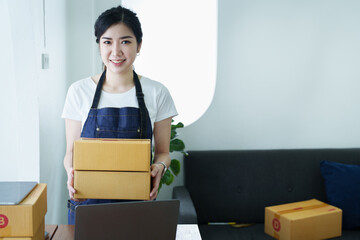 Starting small business entrepreneur of independent Asian woman smiling using computer laptop with cheerful success of online marketing package box items and SME delivery concept