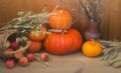 Autumn vibes. Holiday thanksgiving altar with pumpkins, wax candles, wheat spikelets, daisies, apples and pottery on wooden background, selective focus.