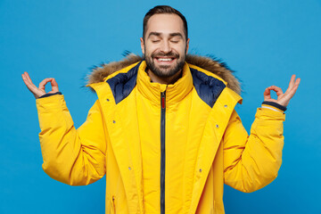 Young spiritual man 20s wearing yellow down jacket hold spread hands in yoga om aum gesture relax...