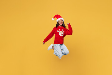 Merry cool little kid teen girl 13-14 years old wear red xmas sweater with deer Santa hat posing jump high do winner gesture isolated on plain yellow background. Happy New Year 2023 holiday concept.