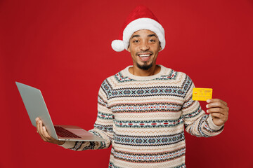 Merry fun young man wear Christmas sweater Santa hat posing use laptop pc computer credit bank card...