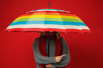 Young woman wears grey sweater scarf cover face with umbrella point index finger aside on area isolated on plain red background studio Healthy lifestyle ill sick disease treatment cold season concept