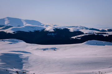 Panoramic view over the ski slope Poiana Brasov ski resort in Transylvania, Pine forest covered in snow on winter season,Mountain landscape in winter with the Bucegi Mountains in the background.