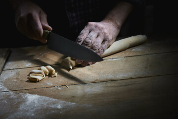 Crop cook cutting pasta dough into pieces with knife