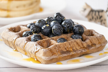 Belgian waffles with fruits berries and honey maple syrup set on white cafe table.
