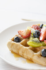 Belgian waffles with fruits berries and honey maple syrup set on white cafe table.
