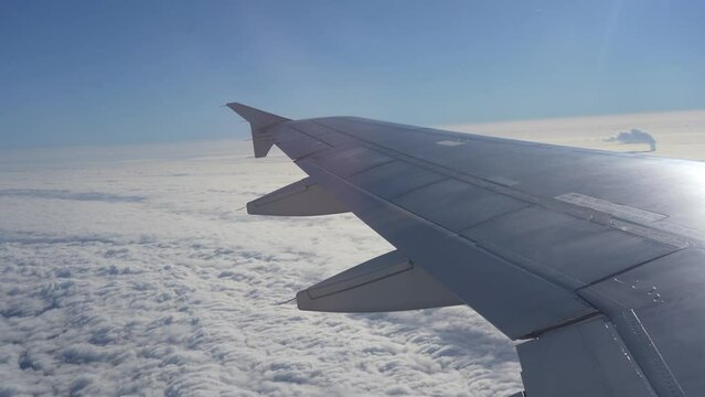 Airplane view through onboard window during flight above clear blue sky with nice white clouds and wing