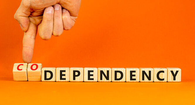 Codependency or dependency symbol. Concept words Codependency and dependency on wooden cubes. Psychologist hand. Beautiful orange background. Psychological codependency dependency concept. Copy space.