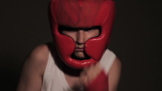 Young guy boxer in a red protective helmet posing at the camera close-up in bandages