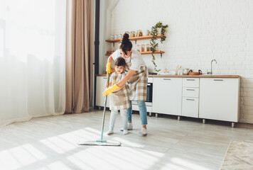 a little daughter and her mom clean the house, a child washes the kitchen floor, a cute little helper girl cleans the floor with a mop, a happy family cleans the room.