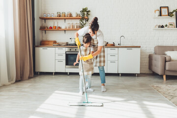 a little daughter and her mom clean the house, a child washes the kitchen floor, a cute little helper girl cleans the floor with a mop, a happy family cleans the room.