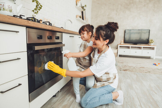 A little girl and her mother are cleaning the kitchen. a woman and a child wipe the oven in the kitchen. house cleaning. helping mom.