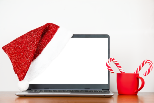 Santa hat on laptop with blank monitor, red cup with candy canes on wooden table, copy space